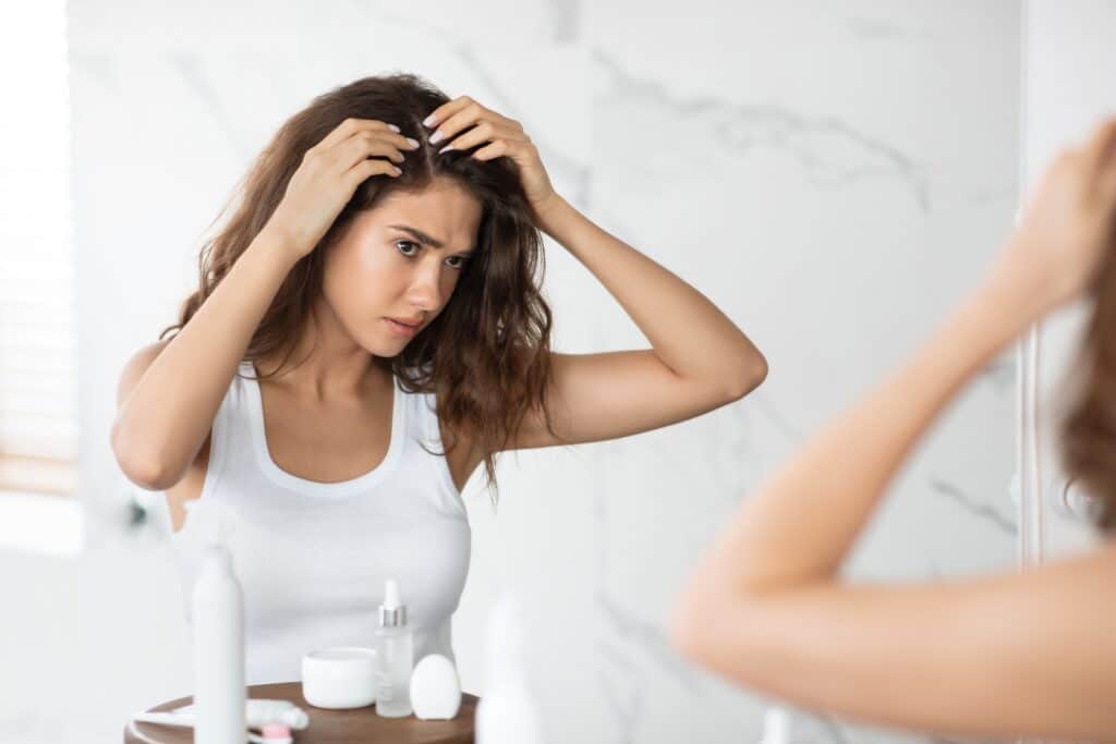 Woman looking in the mirror at her hair loss in need of hair restoration treatment